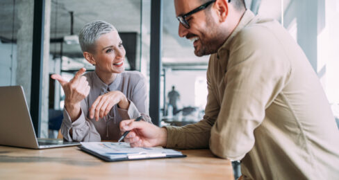 Two business people sitting at a desk in an office and discussing ideas.
