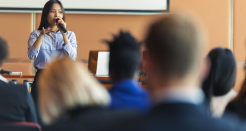 A young woman gives a presentations to an audience of business people.