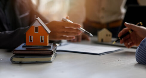 Two people reviewing a contract together, with a small wooden house in the foreground.