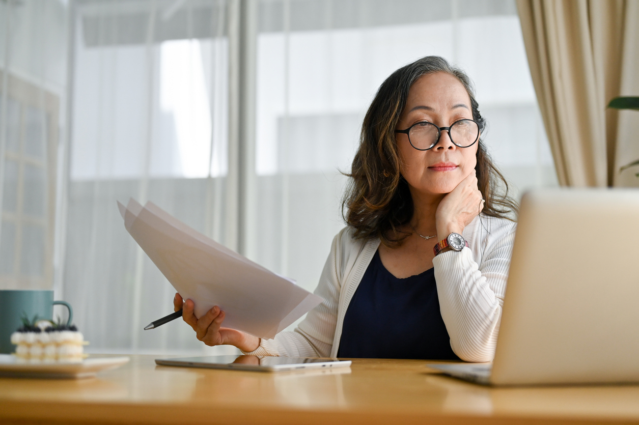 A mid-age business woman holds documents while reading from her laptop computer.