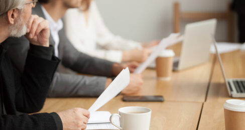 Three business people sit at a conference table and listen to a presentation.