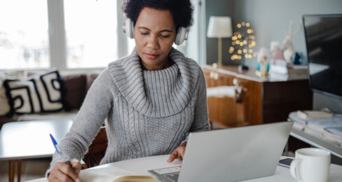 Adult woman taking notes in front of her laptop.