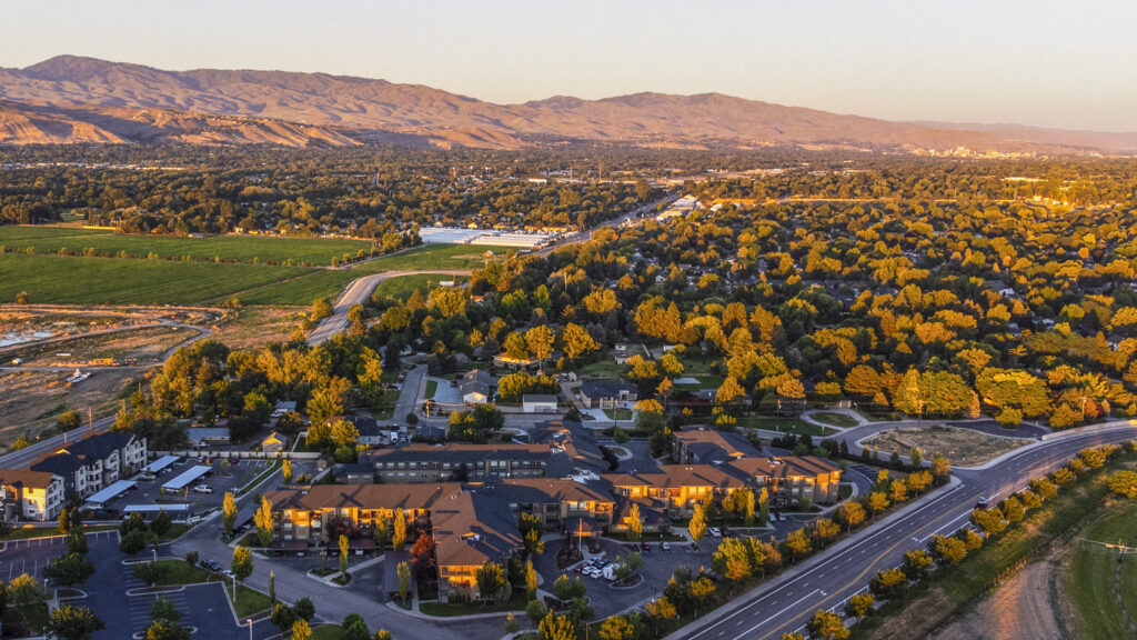 An aerial view of Boise roads and buildings at sunset with hills and leafy trees in the background.