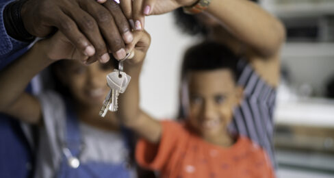 Two parents and their two children pose together, holding up the keys to their new home.