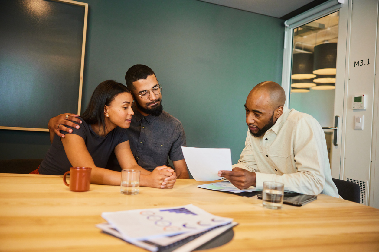 A financial advisor explaining mortgage loan paperwork to a young couple.