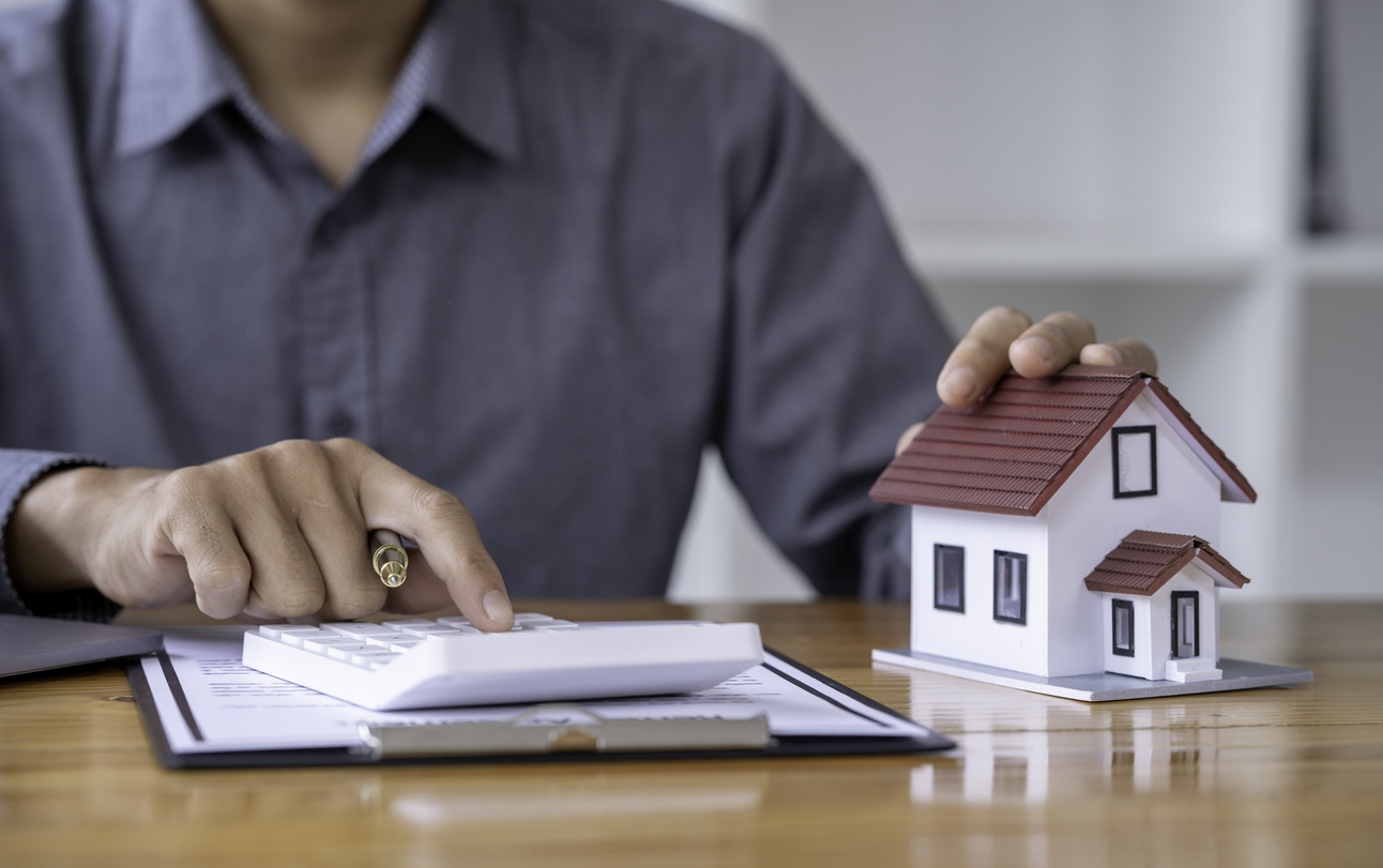 A man calculates housing payments with a small wooden house on the desk.