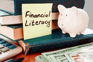 Financial Literacy image of a piggy bank on a desk with a calculator and $100 bills.