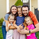 Happy family of 5 hugging outside their home.